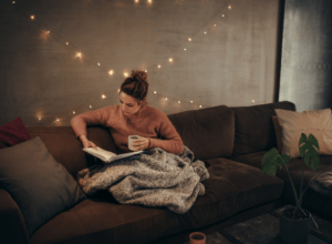 Woman in a cozy position reading a book on the couch. 